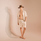 Person wearing a hat and beige shirt and shorts against a beige background