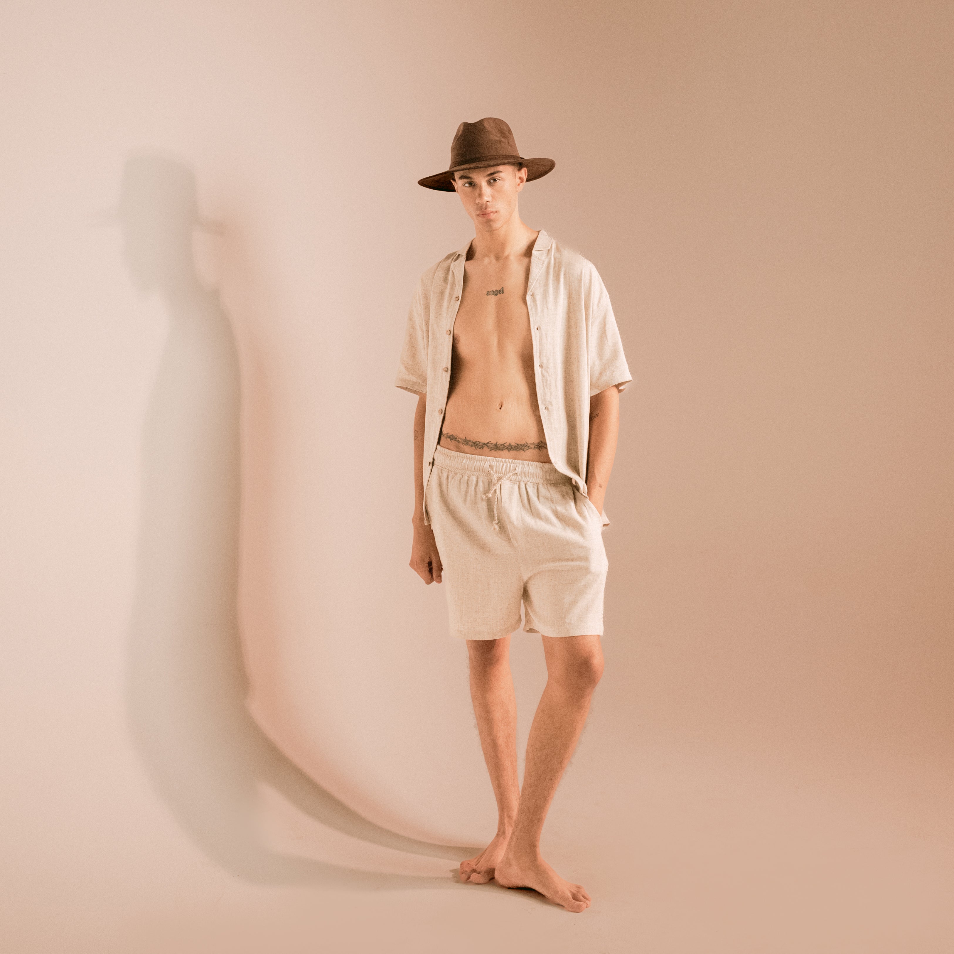 Person wearing a hat and beige shirt and shorts against a beige background