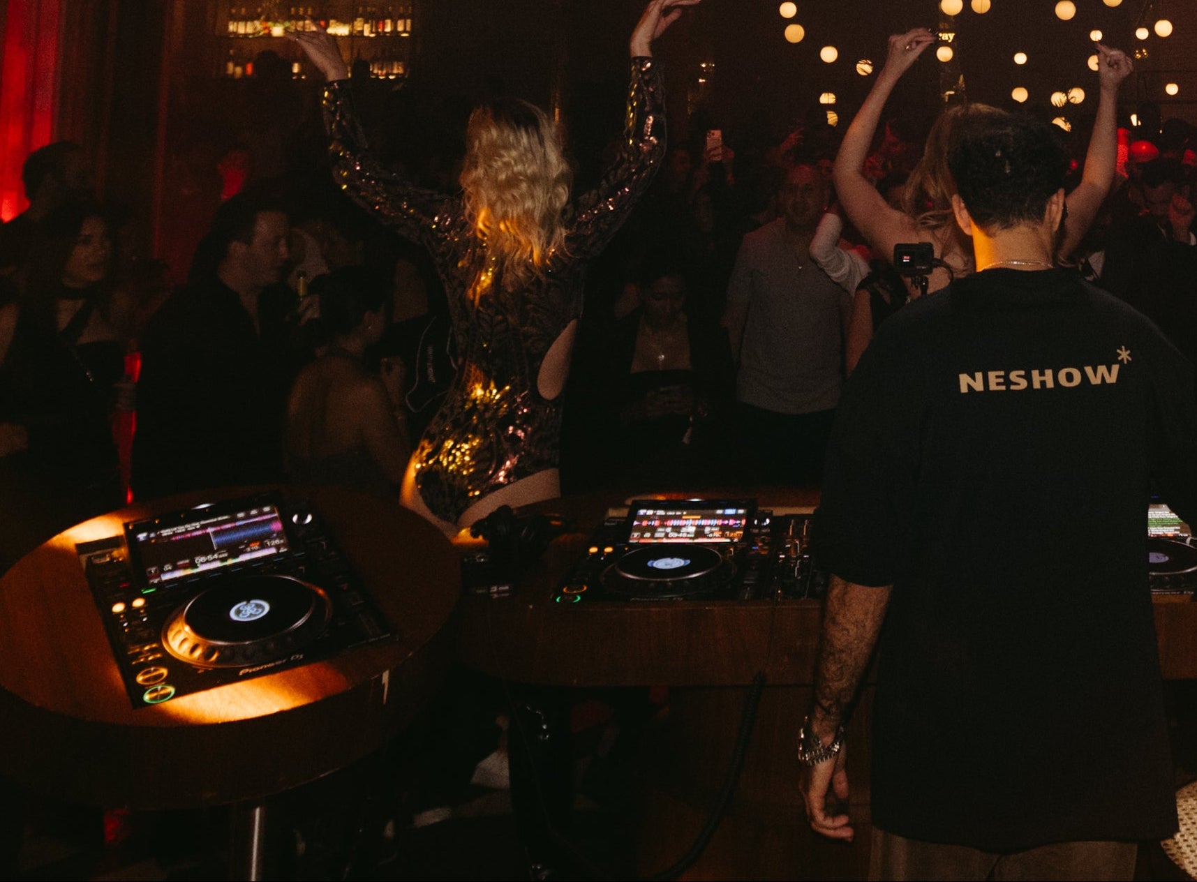 DJ at a club with red lighting and crowd in the background