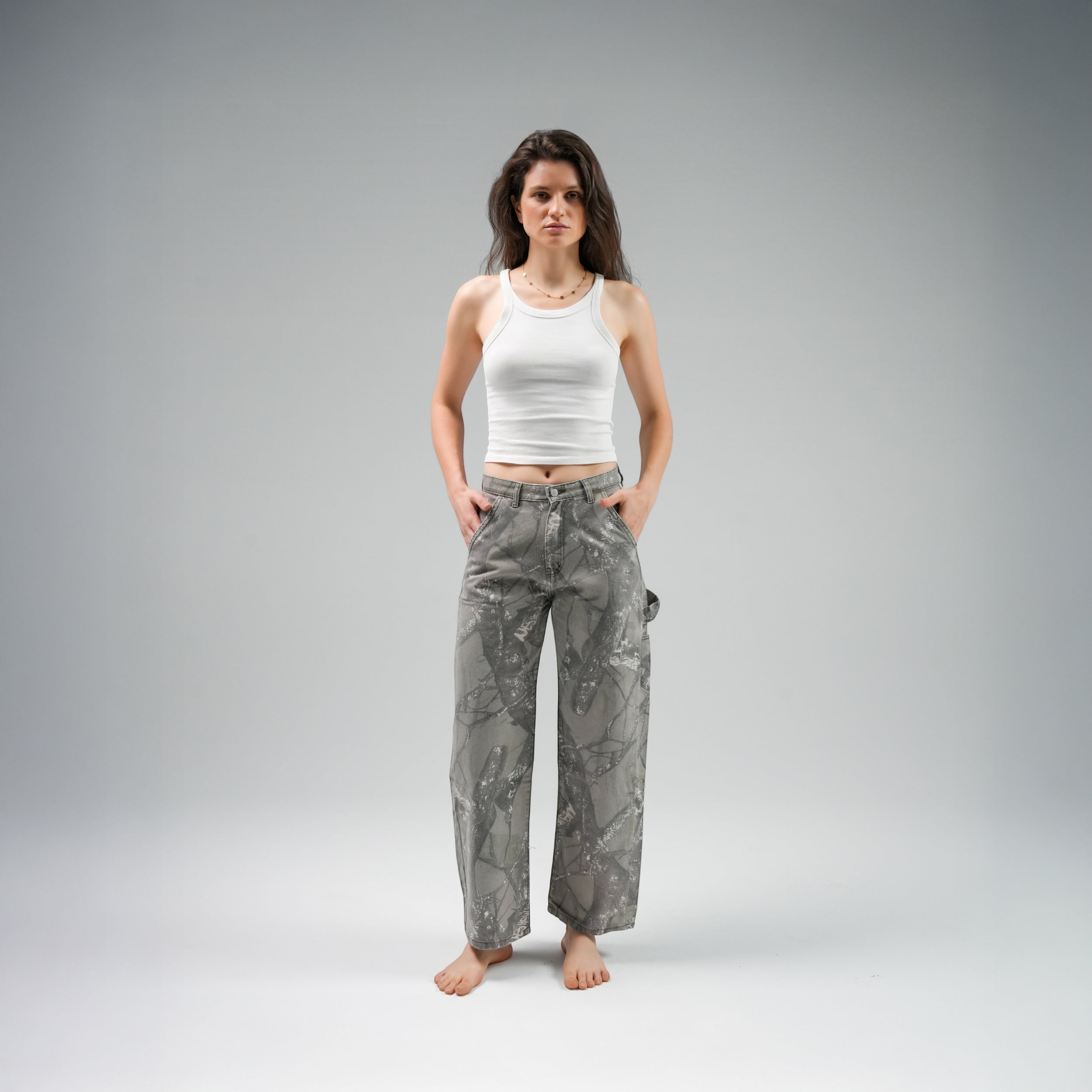 Woman wearing a white tank top and gray patterned pants on a gray background