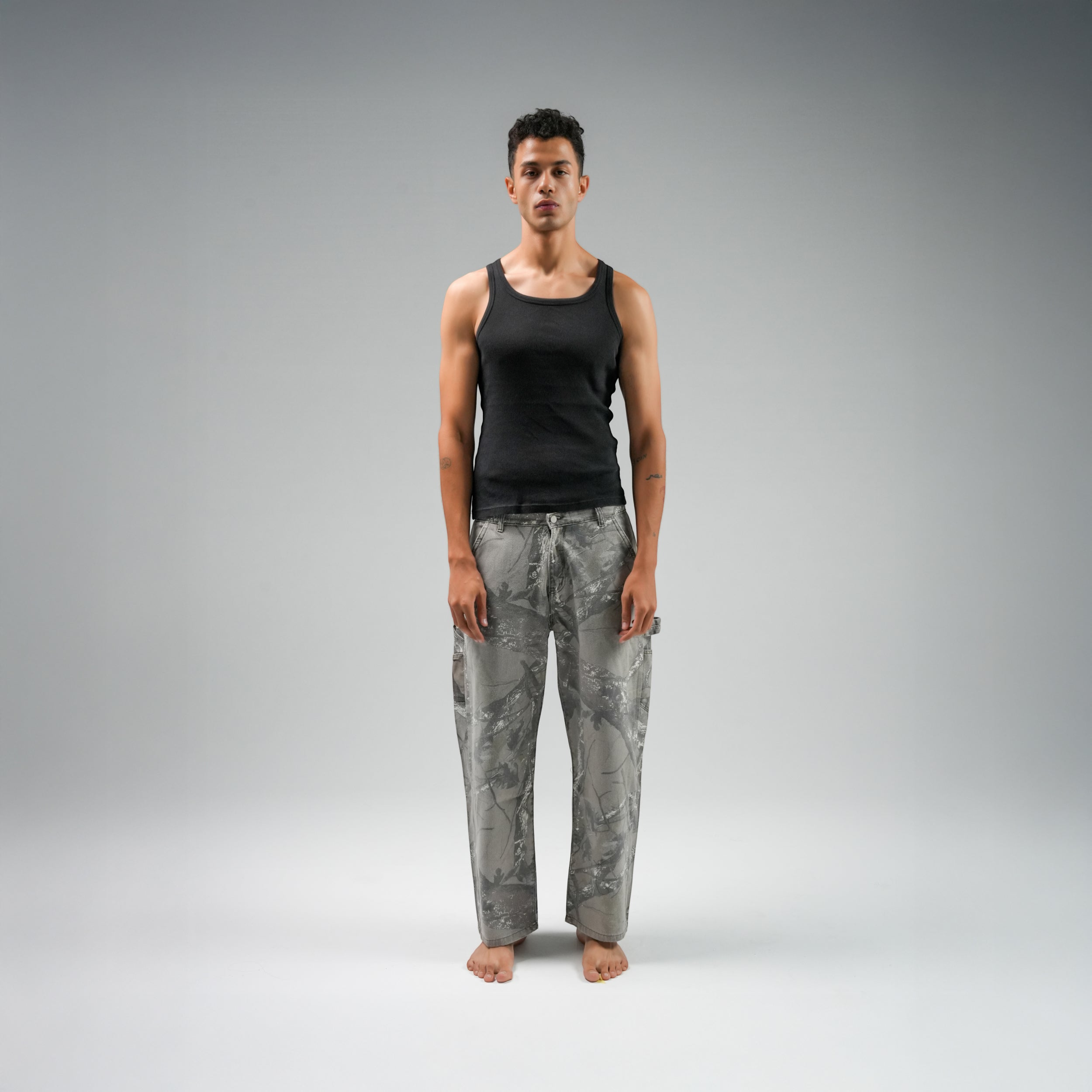 Person wearing a black tank top and gray patterned pants on a gray background