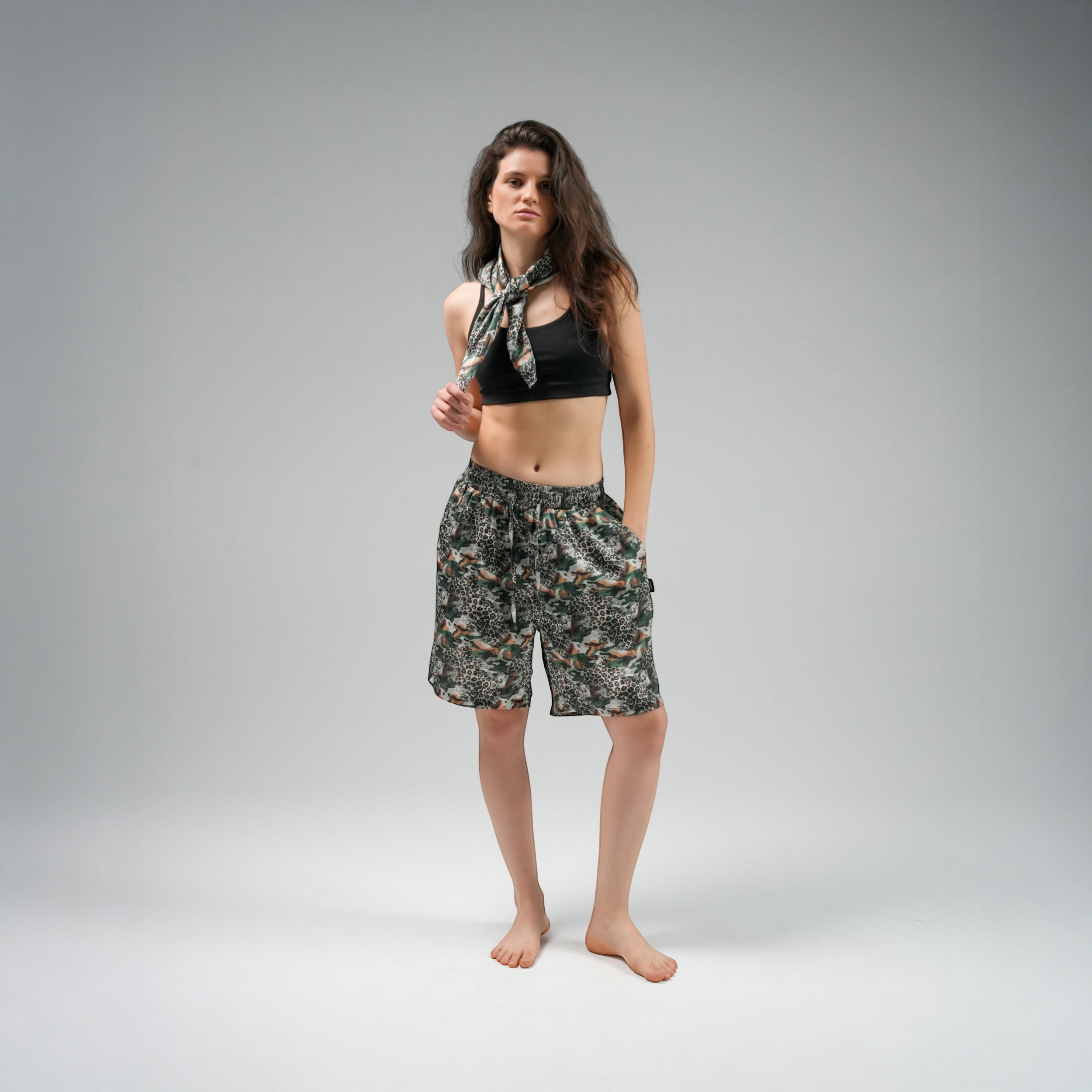 Woman wearing a black crop top and camouflage shorts with a patterned scarf on a gray background